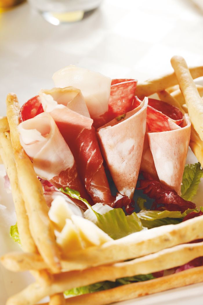 Close-up of Italian prosciutto and breadsticks on a plate, showcasing gourmet presentation.